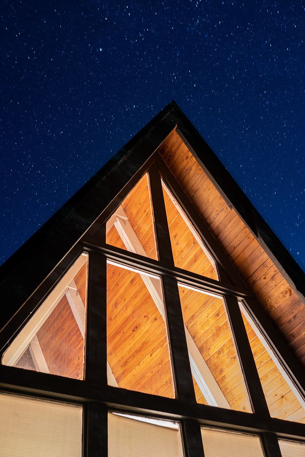 Glass front of an A-frame glowing under a starry sky